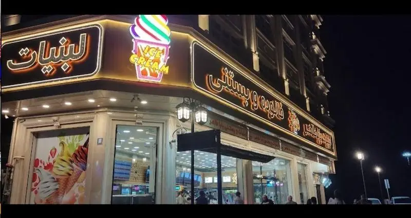 نمای شب فروشگاه لبنیات سنتی باباطاهر با تابلوهای روشن، ارائه دهنده بستنی، فالوده و محصولات لبنی سنتی در محیطی دلنشین.