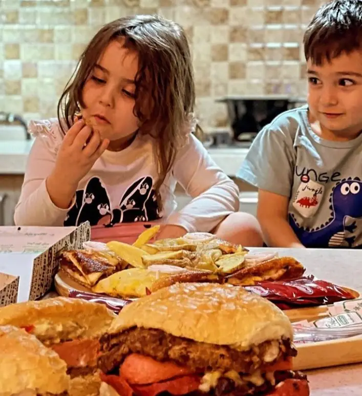 کودکان در عطاویچ فودکورت خلیج فارس مشغول لذت بردن از غذاهای خوشمزه فست فود شامل همبرگر و سیب زمینی سرخ کرده هستند.