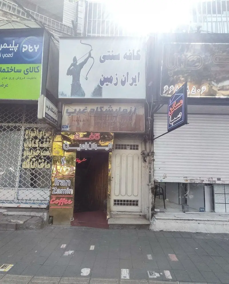 کافه سنتی ایران زمین: نمای ورودی کسب و کار با تابلوی بزرگ تیرانداز، نشان قهوه و سردر طلایی در یک روز روشن.