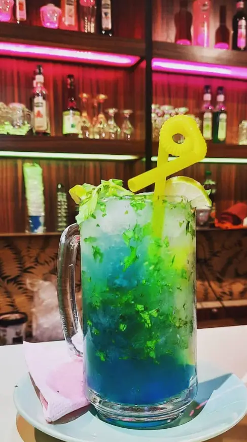 کوکتل یا موکتل آبی و سبز رنگی و دلنشین با برگ نعنا و لیمو در محیط زیبای کافه سنتی ایران زمین، یک انتخاب خنک.