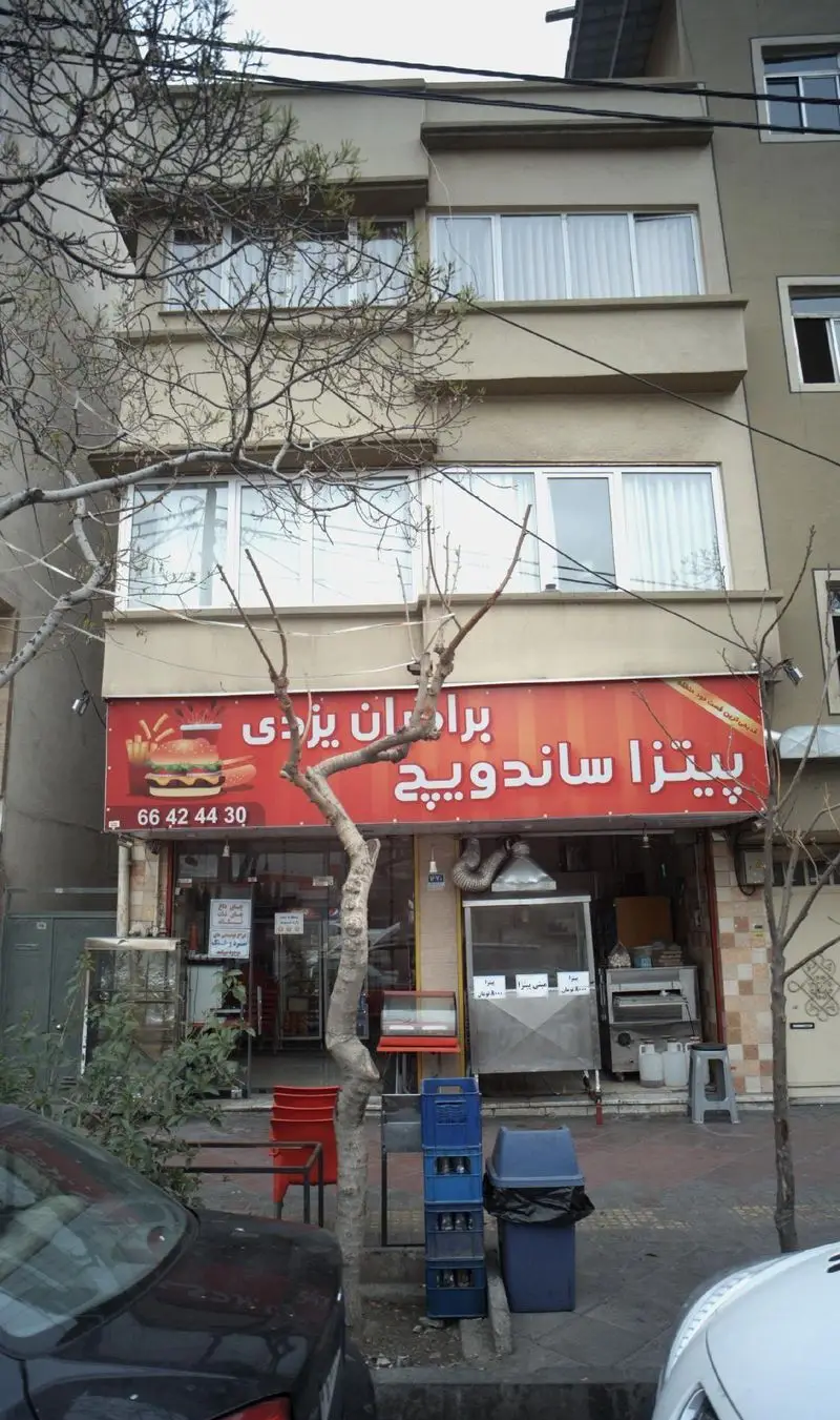 پیتزا ساندویچ برادران یزدی، نمای خارجی مغازه فست فود با تابلوی قرمز شامل تصویر برگر و هات داگ و شماره ۶۶۴۲۴۴۳۰.