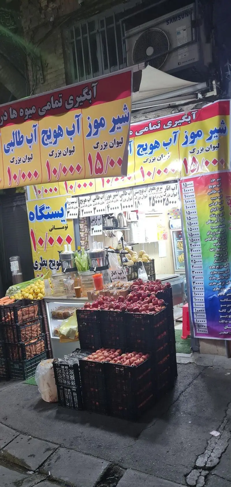 فروشگاه ایستگاه آبمیوه بستنی با تابلوهای قیمت ۱۰ و ۱۵ هزار تومانی، میوه‌های تازه، آب هویج، شیر موز و آب طالبی خوشمزه.