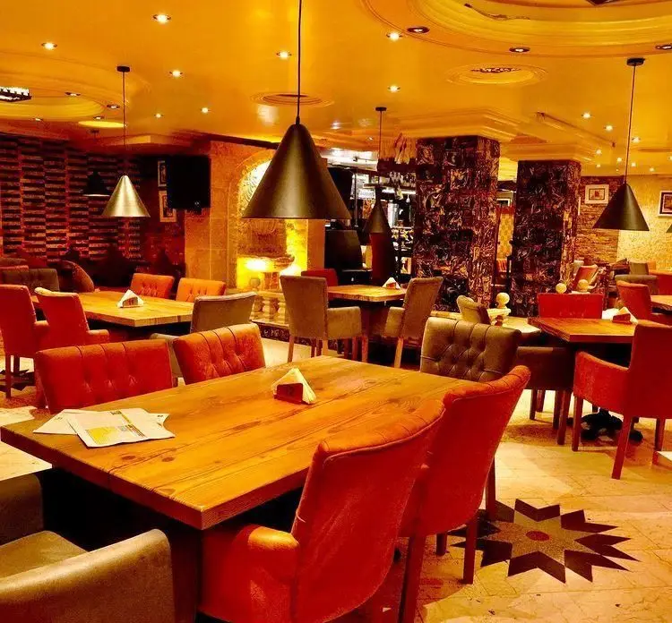 تصویری از کافه رستوران دیاکو، فضایی شیک با میزهای چوبی و صندلی‌های مخملی نارنجی و خاکستری، نورپردازی خاص و دکوراسیون آجری گرم و جذاب.