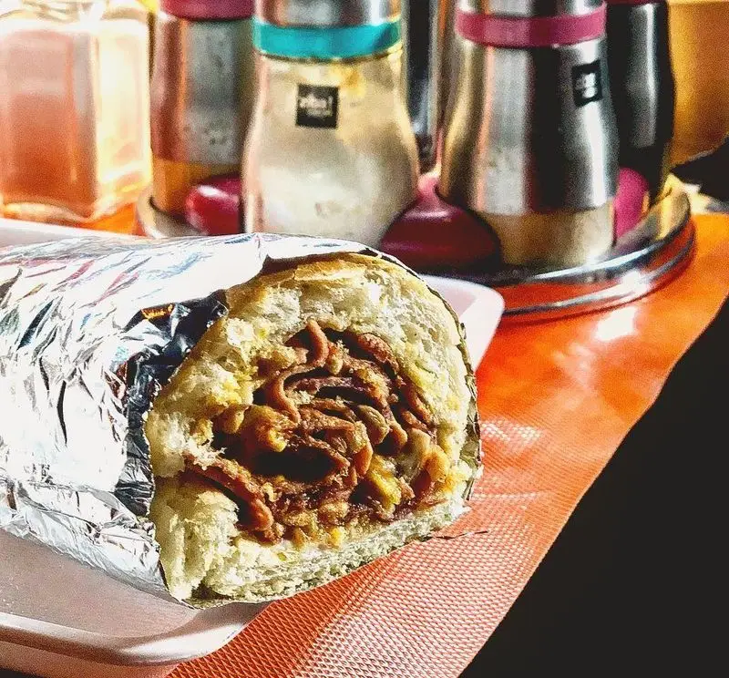 ساندویچ لذیذ و حجیم دونر گوشت یا کباب ترکی فست فود لوبو، نیمه پیچیده در فویل، با پس‌زمینه ادویه‌دان‌ها، آماده برای لذت بردن.