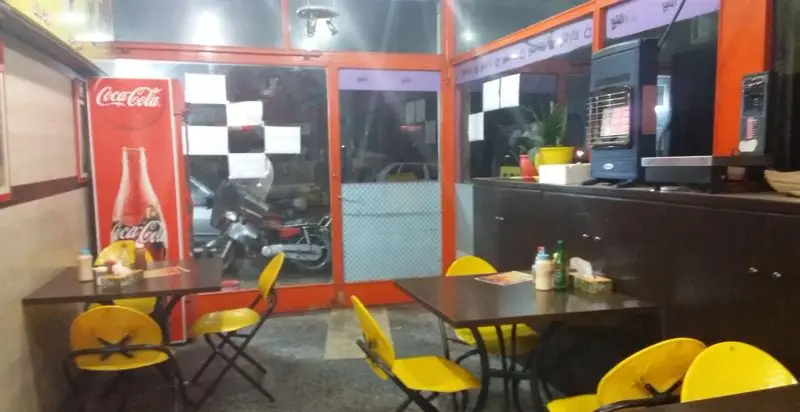 فضای داخلی دنج و دلنشین پیتزا کلبه، شامل میز و صندلی‌های زرد روشن، یخچال کوکاکولا و ویو خیابان، آماده پذیرایی از مشتریان.