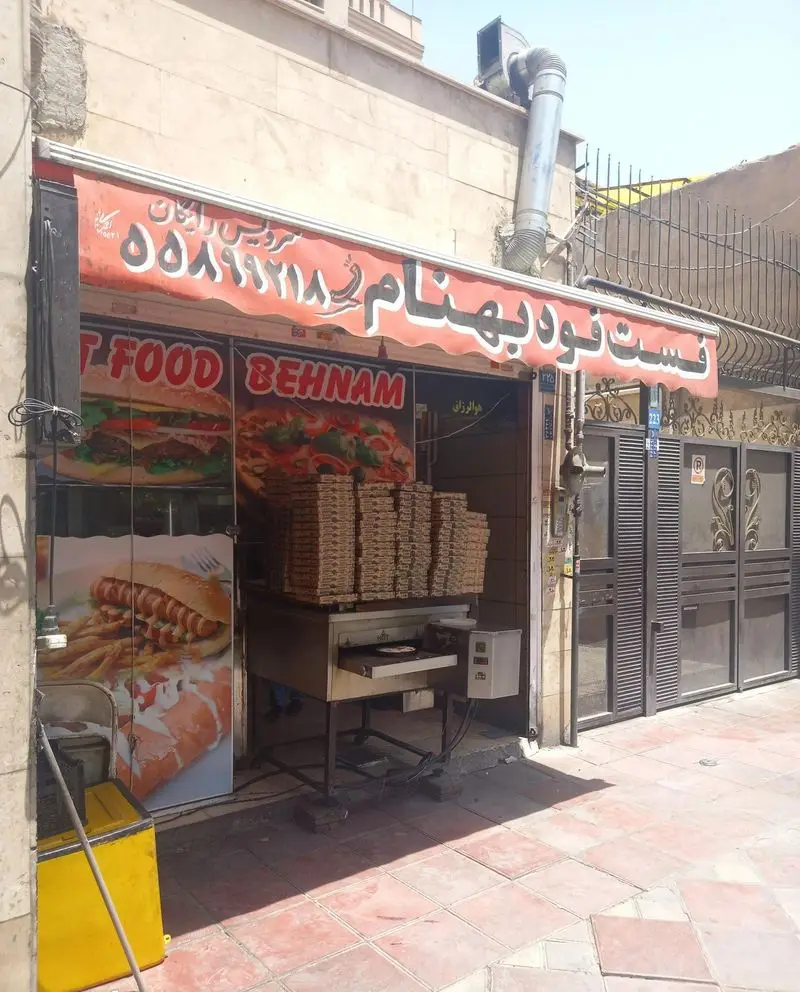 تصویر نمای جلوی فست فود بهنام با تابلو و بنرهای بزرگ پیتزا، برگر و هات داگ، به همراه فر پیتزا و جعبه‌های آماده.