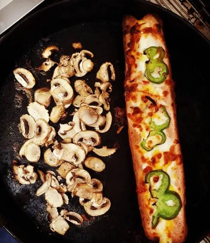فست فود بهنام: نان پیتزا با پنیر آب شده و فلفل سبز، کنار قارچ‌های تازه اسلایس شده در تابه چدنی. غذایی لذیذ و آماده.