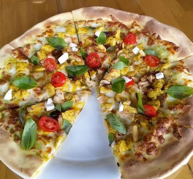 پیتزا مرغ کاری لذیذ با تزئین گوجه گیلاسی، پنیر و برگ‌های ریحان سبز تازه از کافه رستوران لی وان. یک انتخاب عالی!