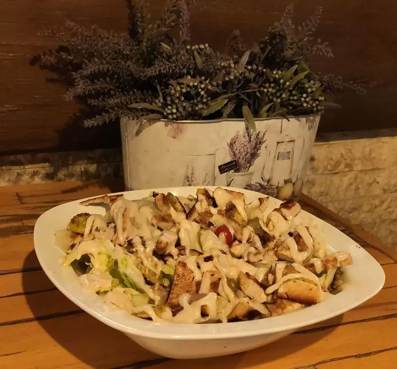 سالاد سزار تازه و دلپذیر کافه رستوران لی وان با مرغ گریل طعم‌دار، برگ کاهو، نان تست و سس مخصوص، انتخابی عالی برای یک وعده سالم.