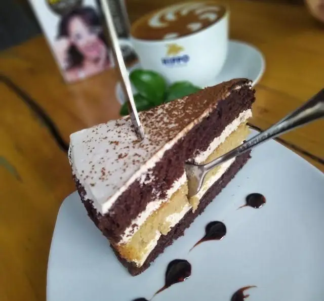 برش کیک شکلاتی خوشمزه با لایه‌های خامه و قهوه با لاته آرت در کافه رستوران لی وان، تجربه‌ای شیرین و دلنشین.