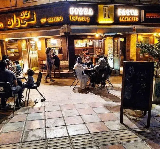 کافه رستوران لی وان در شب با نورپردازی گرم، ارائه دهنده پیتزا و پاستا. مشتریان در فضای داخلی و فضای باز از غذا لذت می‌برند.