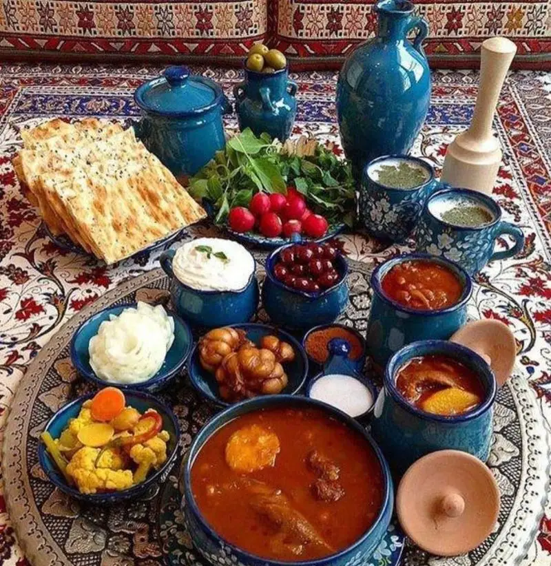 چیدمان زیبای غذای سنتی ایرانی در سفره‌ای رنگارنگ؛ شامل خورش‌های خوش‌رنگ، نان داغ، سبزی تازه، زیتون و ترشی در رستوران طریقت شریعتی.