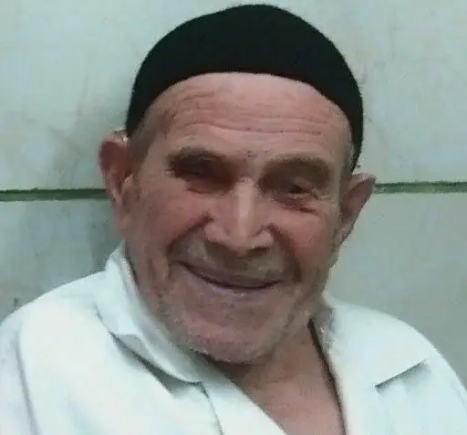 چهره خندان و مهربان حاج ولی، صاحب بستنی و فالوده حاج ولی، که با کلاه مشکی و پیراهن سفید مشغول خوشامدگویی به مشتریان است.