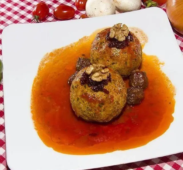 کوفته مخصوص رستوران آجی با سس قرمز خوشرنگ، تزئین شده با گردو و زرشک. تجربه ای اصیل از غذای سنتی ایران.