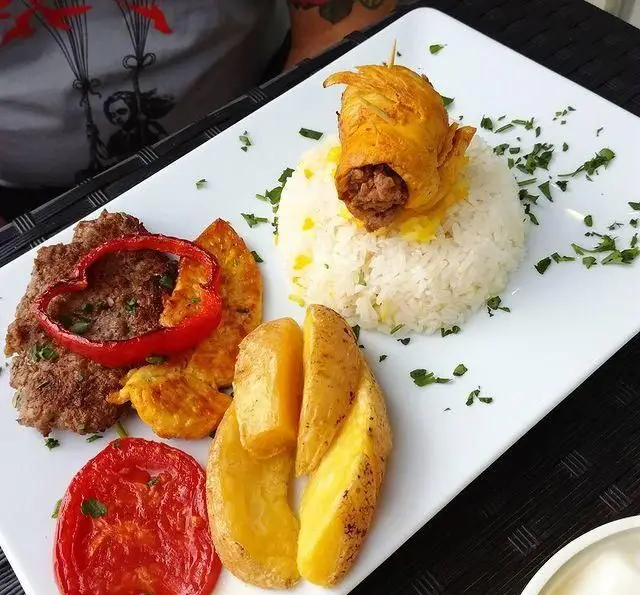 غذای ویژه رستوران آجی: بشقاب کباب کوبیده، برنج زعفرانی با جوجه رول، سیب‌زمینی و گوجه کبابی، تزئین شده با سبزیجات تازه. یک تجربه خوشمزه.