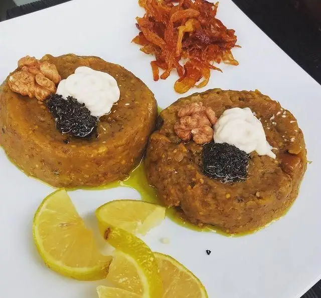 کشک بادمجان سنتی و خوشمزه رستوران آجی، غذای محبوب ایرانی، با تزئین کشک، گردو، نعنا داغ و پیاز داغ فراوان، سرو با لیمو.