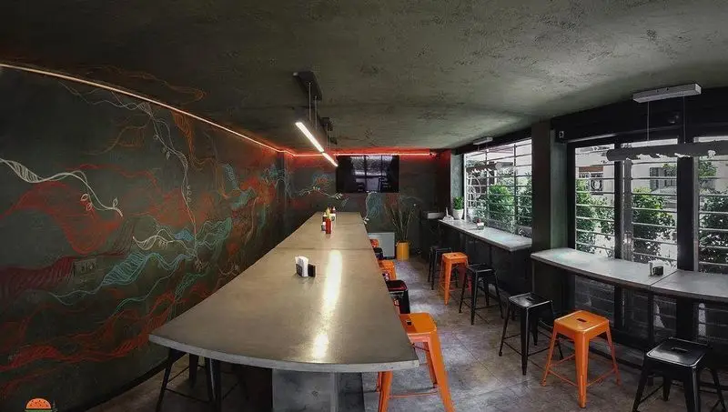 نمایی از فضای داخلی فست فود آربی برگر، با طراحی مدرن، میزهای بلند، صندلی‌های رنگی و نقاشی‌های دیواری خلاقانه برای جذب مشتری.