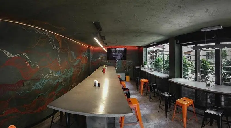 دکوراسیون داخلی مدرن و جذاب فست فود آربی برگر با میز بزرگ اشتراکی، صندلی‌های کانتر نارنجی و مشکی، دیوار هنری و نورپردازی نئون قرمز.