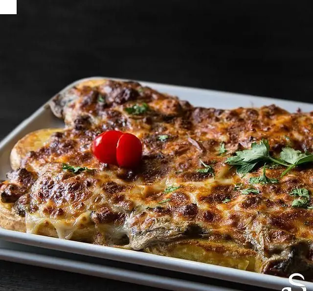 خوراک لذیذ و پنیردار از کافه رستوران هفت آسمان: گراتن طلایی با لایه های پنیری برشته، تزئین شده با گوجه و سبزی تازه.