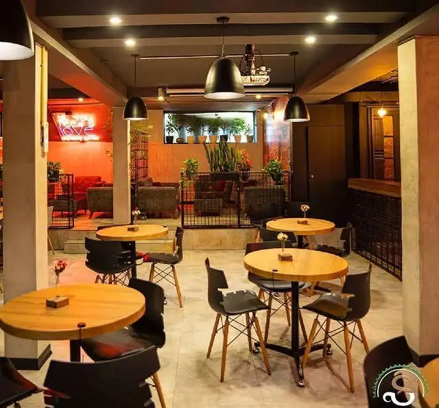 فضای داخلی کافه رستوران هفت آسمان با دکوراسیون مدرن و دنج، شامل میز و صندلی‌های چوبی، نورپردازی خاص، نئون Love و گیاهان سرسبز.