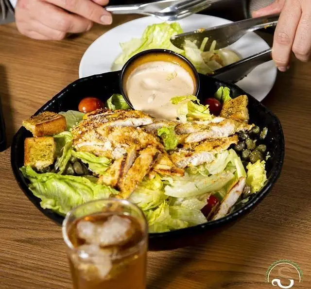 تجربه طعم سالاد سزار مرغ گریل شده تازه، همراه با نان سیر و نوشیدنی خنک در محیط دلنشین کافه رستوران هفت آسمان.