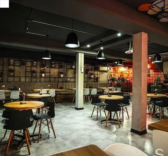 فضای داخلی مدرن و دنج کافه رستوران هفت آسمان، با میز و صندلی‌های چوبی، نیمکت‌های راحت، دکوراسیون دیواری سبز و نورپردازی ملایم.