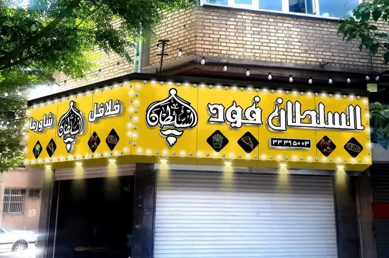 تابلوی زرد و پرنور کسب و کار "السلطان فود" با لوگوی خاص، معرفی فلافل، شاورما، پیتزا و ساندویچ‌های متنوع، شماره تماس: ۳۳۳۹۵۰۳.