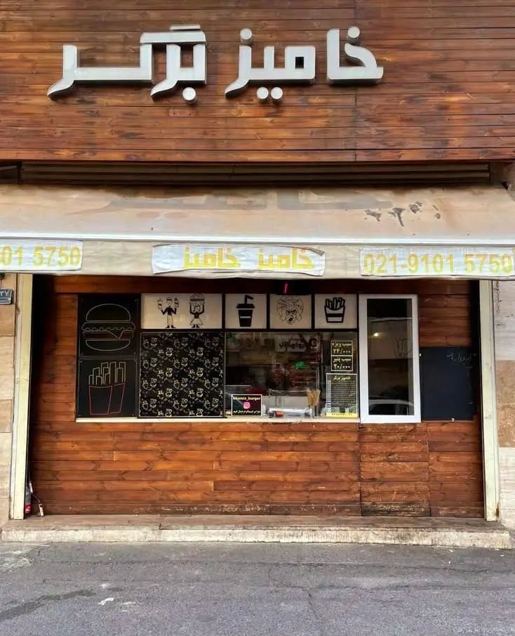 نمای بیرونی جذاب رستوران خامیز برگر در تهران، شامل تابلوی بزرگ و طرح‌های گرافیکی برگر و سیب‌زمینی سرخ‌کرده.