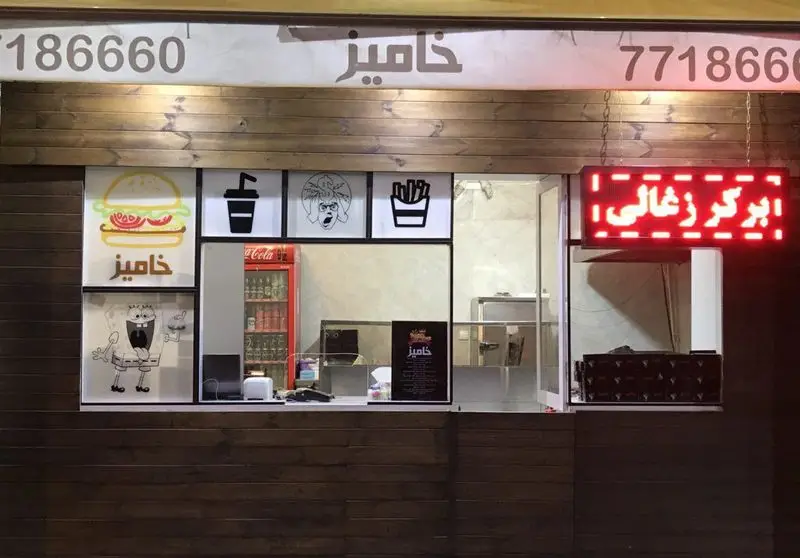 نمای بیرونی فست فود خامیز برگر با تابلو "برگر زغالی"، شماره تماس 77186660 و نمادهای نوشیدنی و سیب زمینی سرخ کرده.
