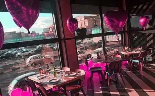 فضای داخلی دنج و مدرن کافه رستوران ویند با میزهای چیدمان شده، بالن‌های قلبی صورتی و چشم‌انداز شهری، مکانی ایده‌آل برای قرارهای عاشقانه و لحظات خاص.