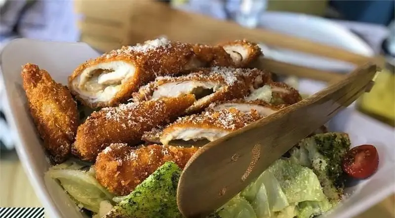 غذای خوشمزه کافه رستوران ویند: فیله مرغ سوخاری شکم پر با پنیر و سس، سرو شده روی سالاد سزار تازه و بروکلی. تجربه‌ای لذیذ از منوی ویند.