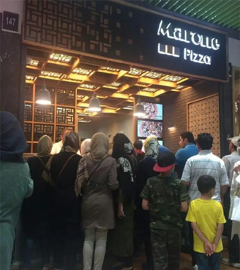 نمای شلوغ فست فود مارونه پیتزا، همراه با مشتریان در صف سفارش غذا. تابلوی نام و دکوراسیون داخلی جذاب است.
