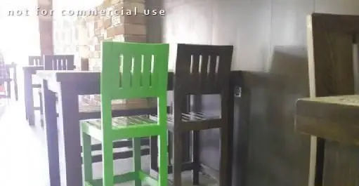 فضای داخلی شیک و مدرن کافه شیک شک با میزهای چوبی تیره و صندلی‌های بلند، شامل یک صندلی سبز روشن، محیطی دلنشین برای مشتریان.