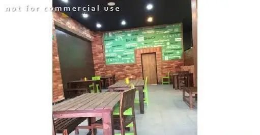 فضای داخلی رستوران شیک شک: دکوراسیون جذاب با دیوارهای آجری، تابلوی منوی سبز، و چیدمان میز و نیمکت‌های چوبی و صندلی‌های سبز.