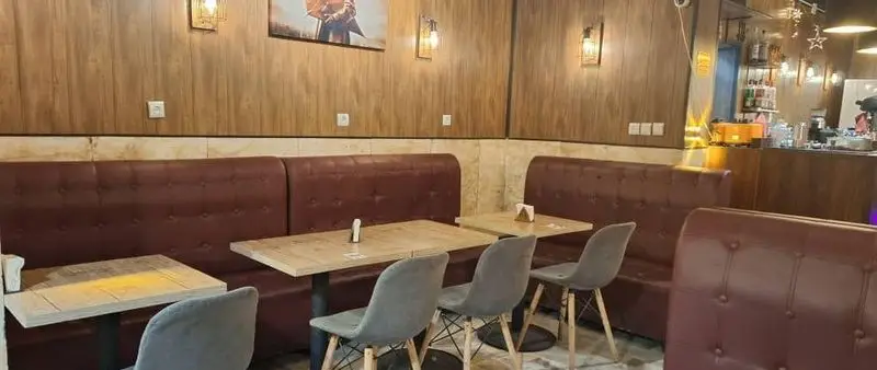 فضای داخلی کافه آگات با دکوراسیون شیک، مبلمان راحتی چرم قهوه‌ای، میزهای چوبی و نورپردازی دلنشین، محیطی دنج و عالی برای تجربه‌ای به‌یادماندنی.