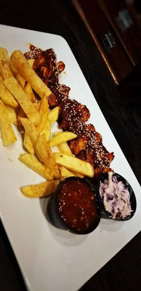 بال مرغ کنجدی با سس BBQ، سیب زمینی سرخ کرده و سالاد کلم تازه سرو شده در محیط دلنشین کافه آگات