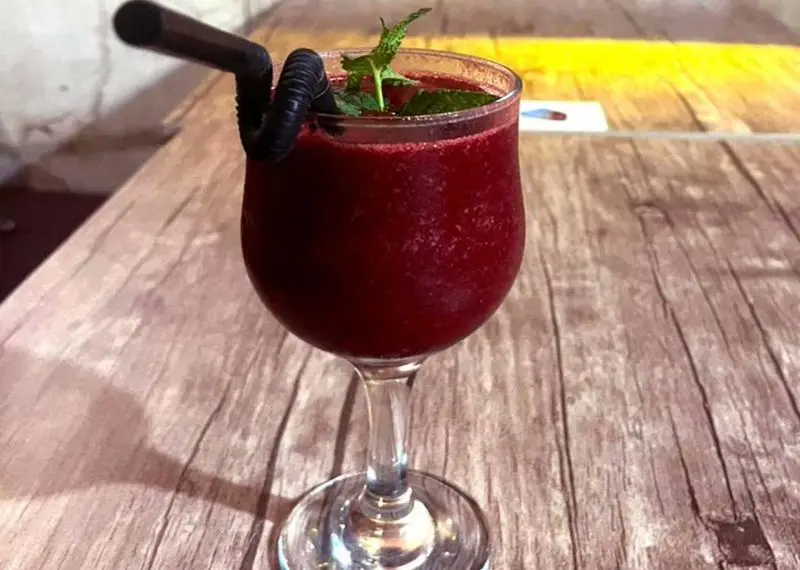 اسموتی قرمز خنک و جذاب کافه آگات با تزئین برگ نعنا و نی مشکی، نوشیدنی دلچسب روی میز چوبی برای لحظات آرام.