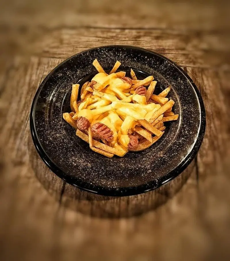 سیب زمینی سرخ کرده با سس پنیر آب شده و تکه‌های هات داگ سرو شده در بشقاب مشکی کافه آگات، لذت‌بخش و اشتهاآور.