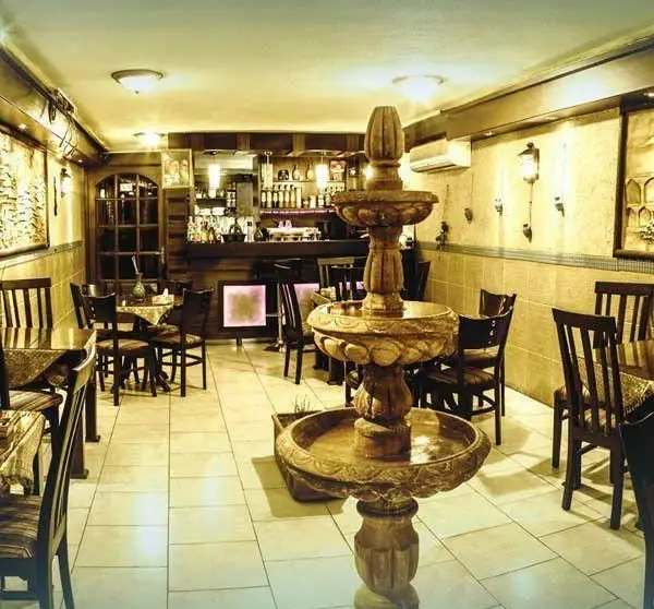 فضای داخلی دنج و شیک کافه میامی با فواره سنگی زیبا، میز و صندلی‌های چوبی و بار کامل در پس زمینه، محیطی دلنشین و آرامش‌بخش.