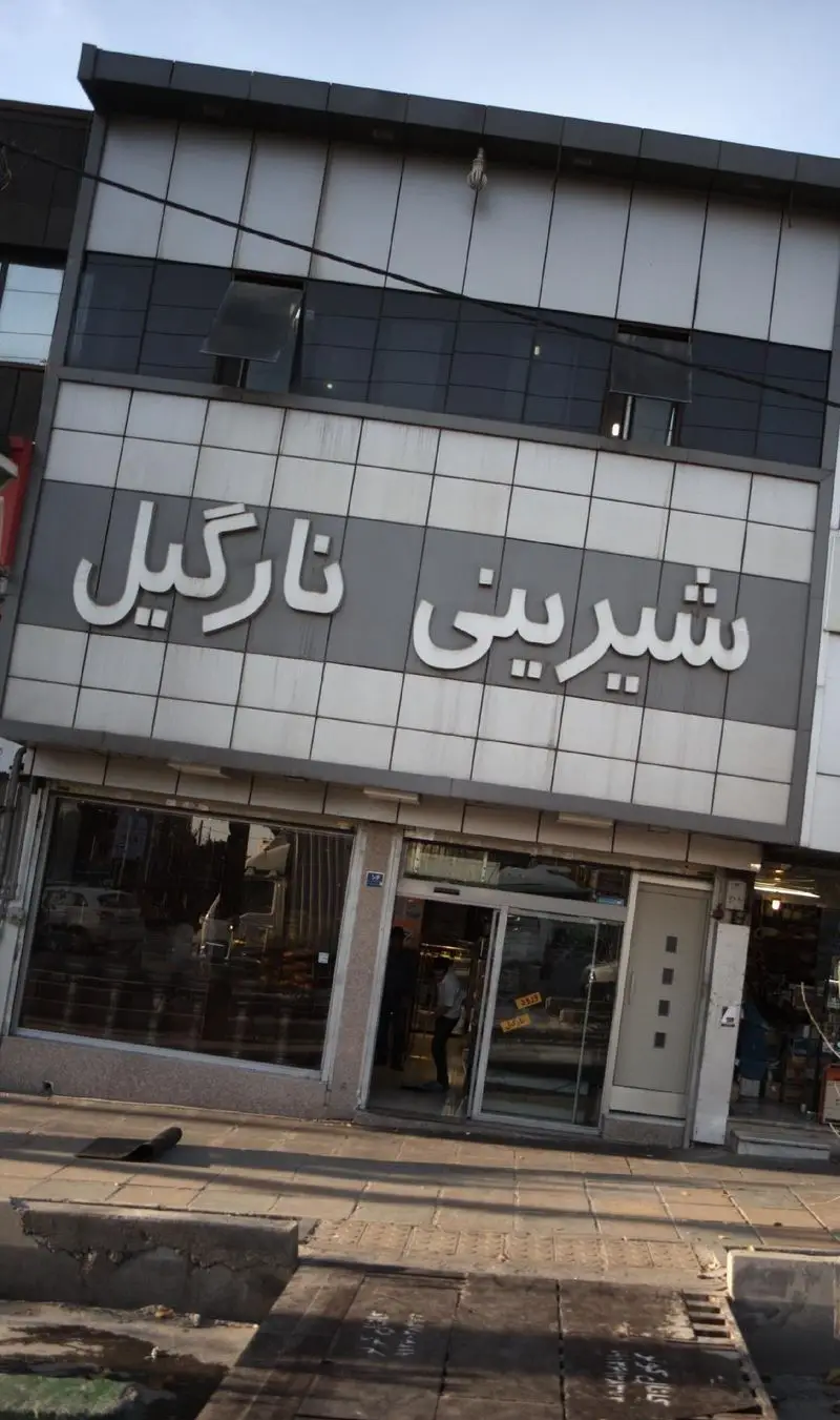 نمای بیرونی ساختمان قنادی شیرینی نارگیل در خیابان، با تابلوی بزرگ و روشن و ویترین جذاب برای خرید انواع شیرینی و دسر.