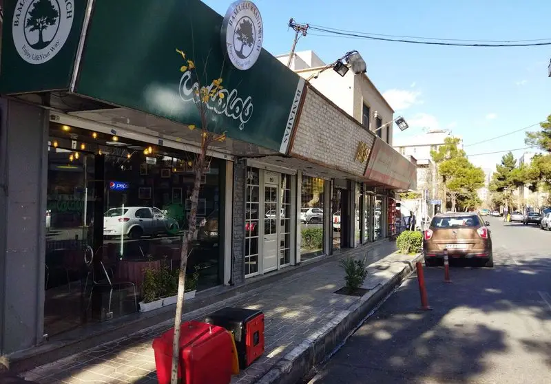 نمای بیرونی مغازه ساندویچ باماهاس، فست فود معروف با تابلو سبز رنگ و لوگوی درخت، در کنار پیاده‌رو خیابان.