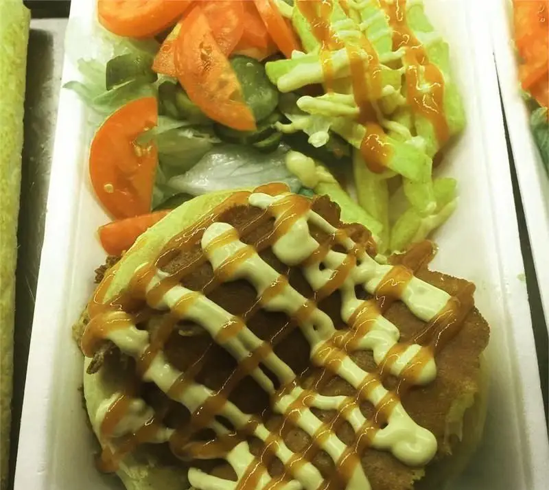 ساندویچ برگر ویژه بام برگر با سس‌های مخصوص، کنار سالاد تازه گوجه و کاهو و سیب‌زمینی یا سبزیجات سرخ شده در ظرف یکبار مصرف.