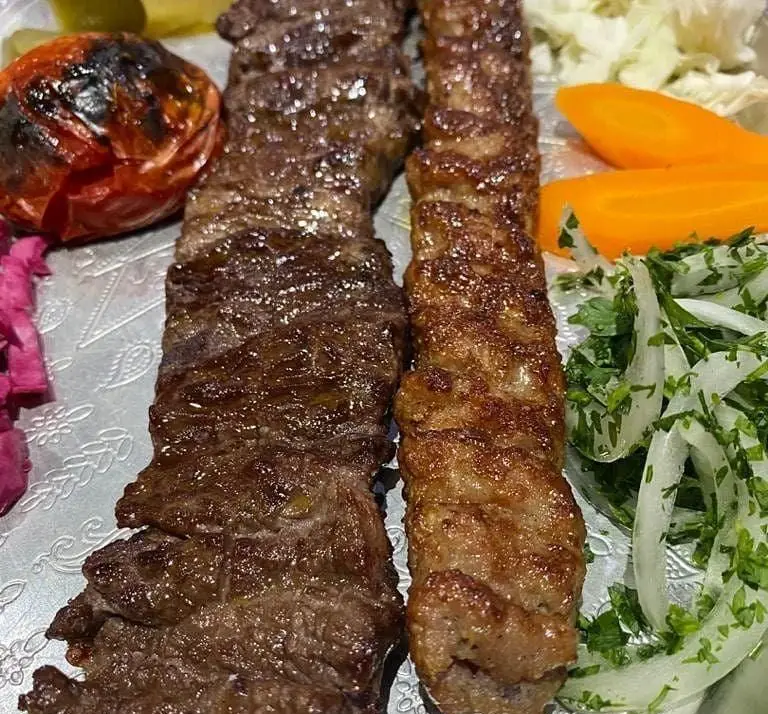 کباب برگ و کوبیده در رستوران بام شهران، با گوجه کبابی، سالاد پیاز و سبزی، ترشی و هویج. یک غذای لذیذ ایرانی.