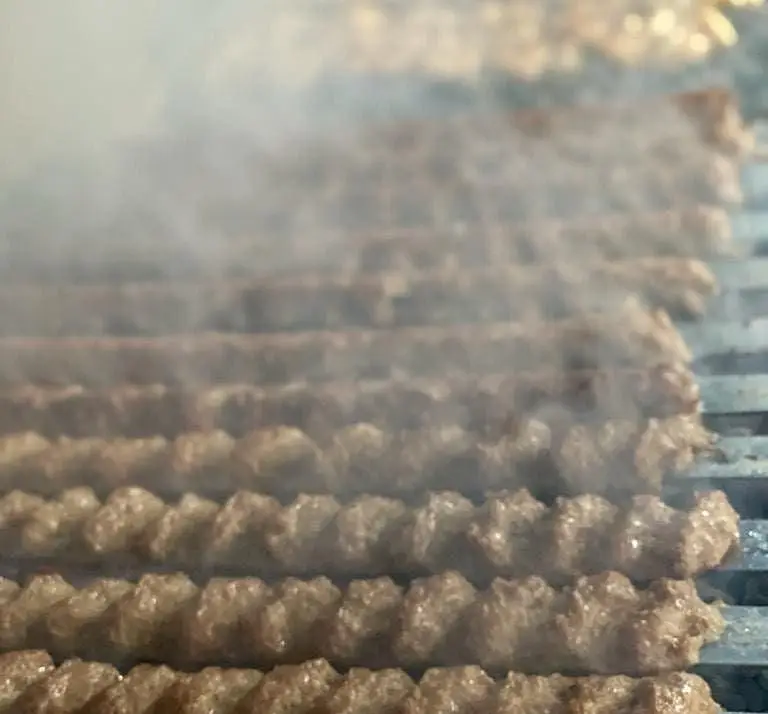 کباب کوبیده تازه و آبدار در حال پخت روی آتش در رستوران بام شهران، تجربه‌ای بی‌نظیر از طعم اصیل کباب ایرانی.