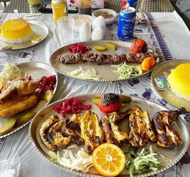 نمایی از میز غذای رنگارنگ رستوران بام شهران با کباب کوبیده، جوجه کباب، برنج قالبی زعفرانی، گوجه و خیارشور.