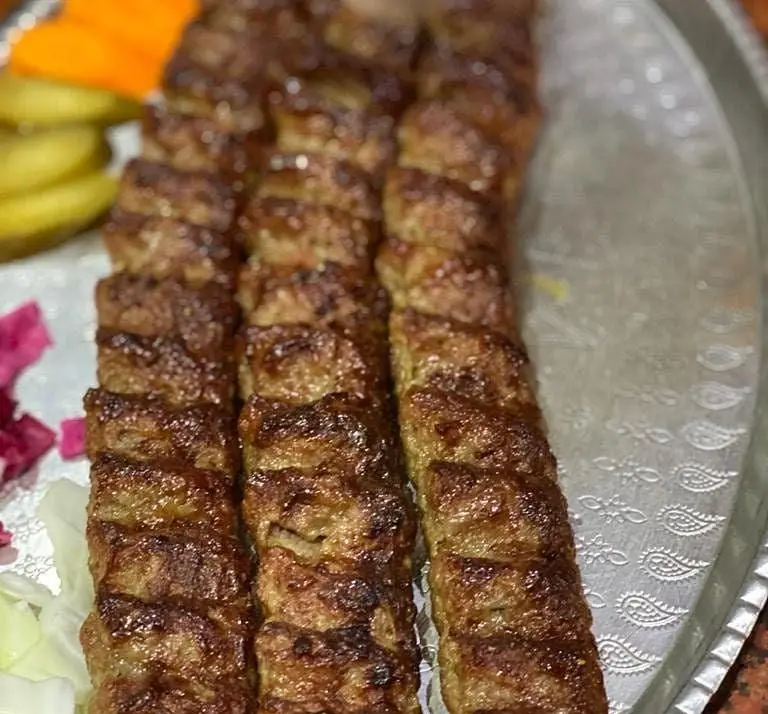 کباب کوبیده لذیذ و آبدار رستوران بام شهران، سرو شده روی سینی با ترشی، هویج و کاهو، تجربه غذایی خوشمزه.