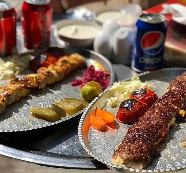 میز غذای دلپذیر رستوران بام شهران: کباب کوبیده، جوجه کباب، گوجه کبابی، دورچین و نوشیدنی‌های خنک در فضایی عالی.