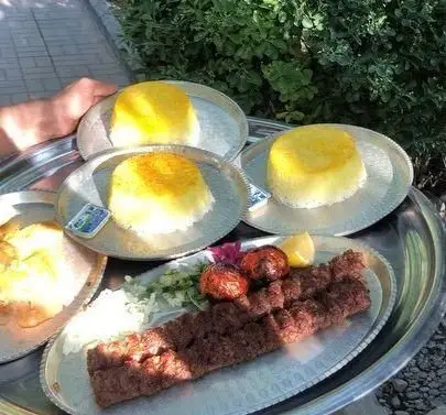 چلو کباب کوبیده لذیذ رستوران بام شهران با برنج زعفرانی، گوجه کبابی و کره. یک وعده غذای سنتی و خوشمزه ایرانی در فضای باز.