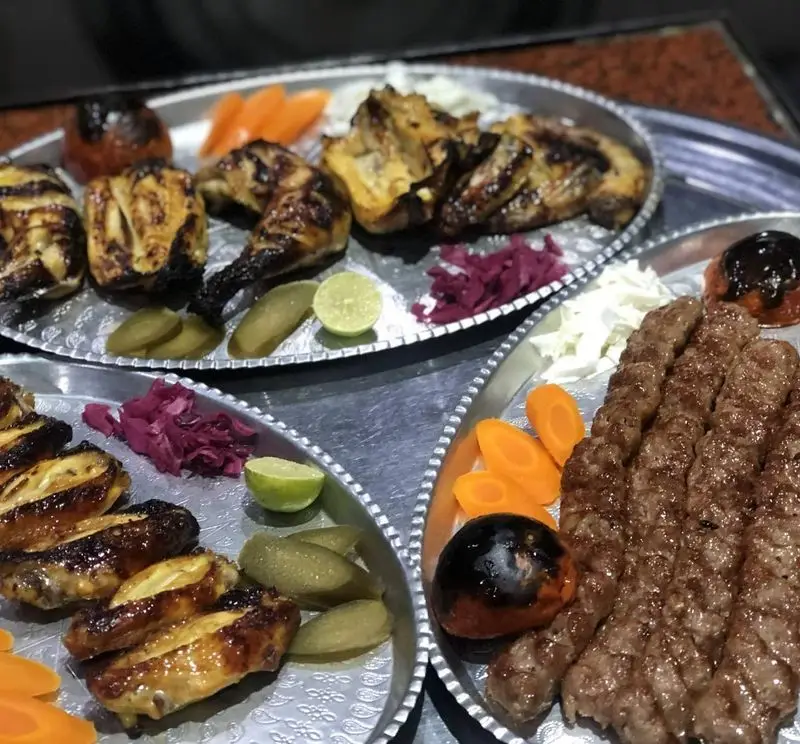 انواع کباب ایرانی شامل کوبیده، مرغ و بال کبابی خوشمزه با دورچین تازه (هویج، خیارشور، گوجه کبابی و لیمو) در رستوران بام شهران.