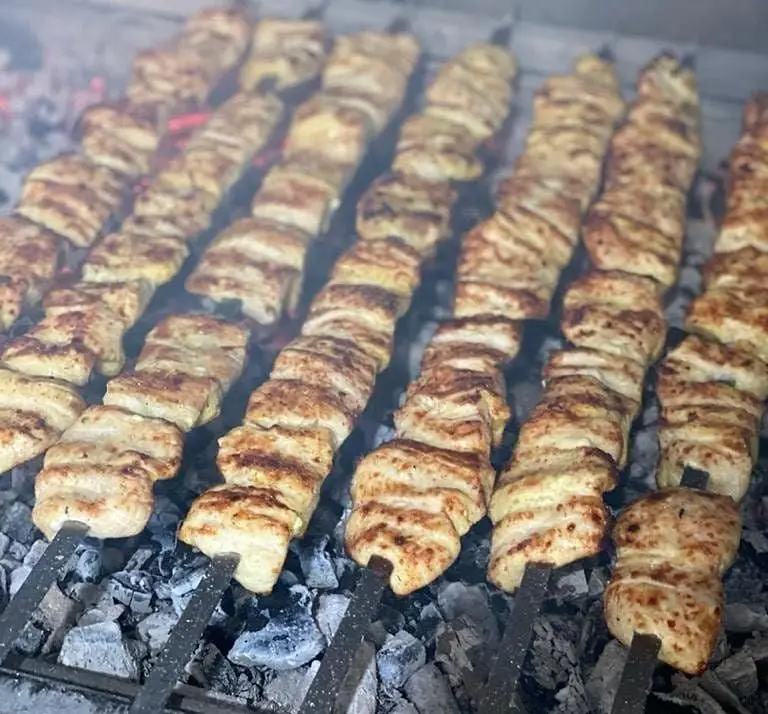 نمایی از جوجه کباب‌های لذیذ و دست‌ساز رستوران بام شهران در حال پخت بر روی ذغال گداخته. طعم بی‌نظیر و کیفیت عالی.
